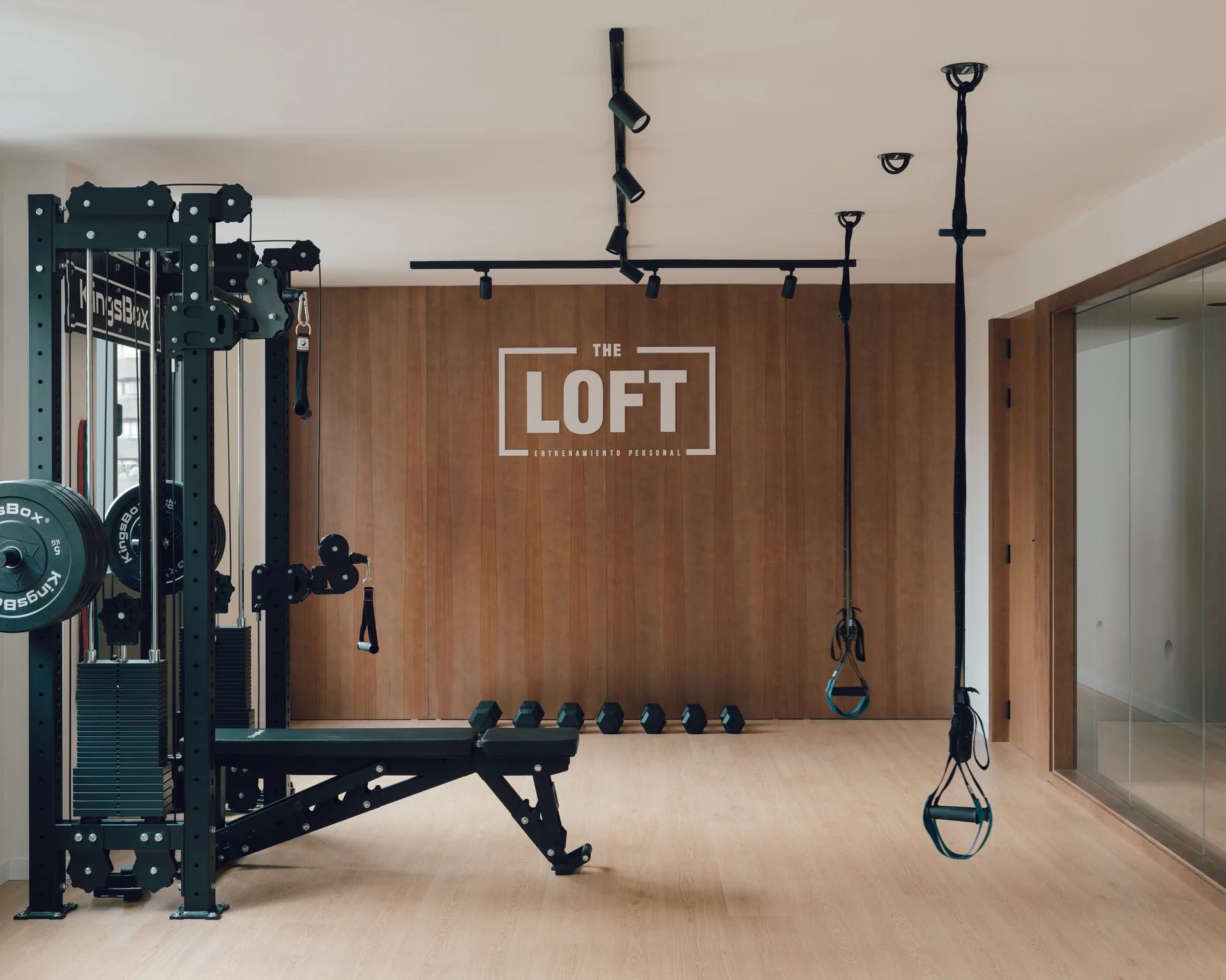Estudio The Loft en Gandía, con estación de poleas, banco y pared de madera con el logo