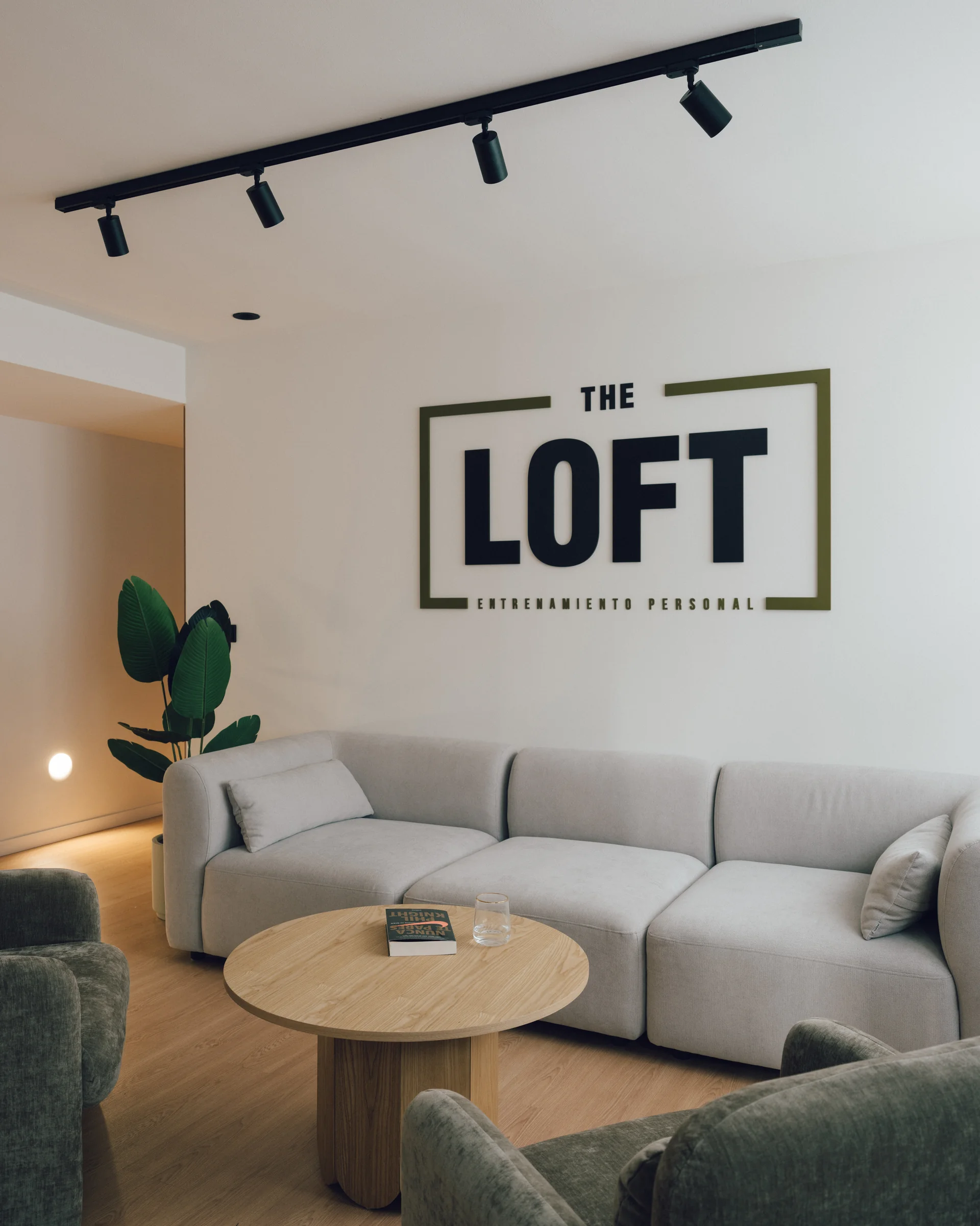 Zona de espera de The Loft, con sofá, butacas y mesa de madera bajo el logo del estudio